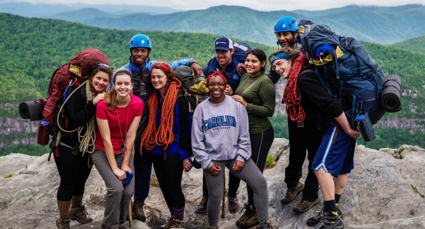 A group of people pose for a photo on a rocky overlook, with the blue ridge mountains below. 